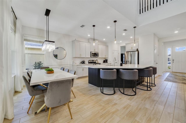 kitchen with white cabinetry, a breakfast bar area, hanging light fixtures, stainless steel appliances, and a center island with sink