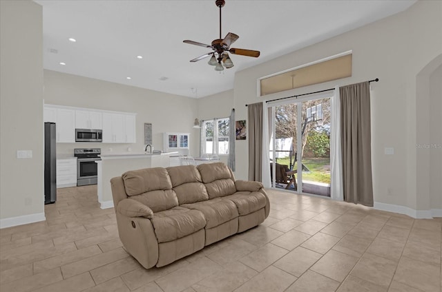 living room featuring light tile patterned flooring, ceiling fan, sink, and a high ceiling