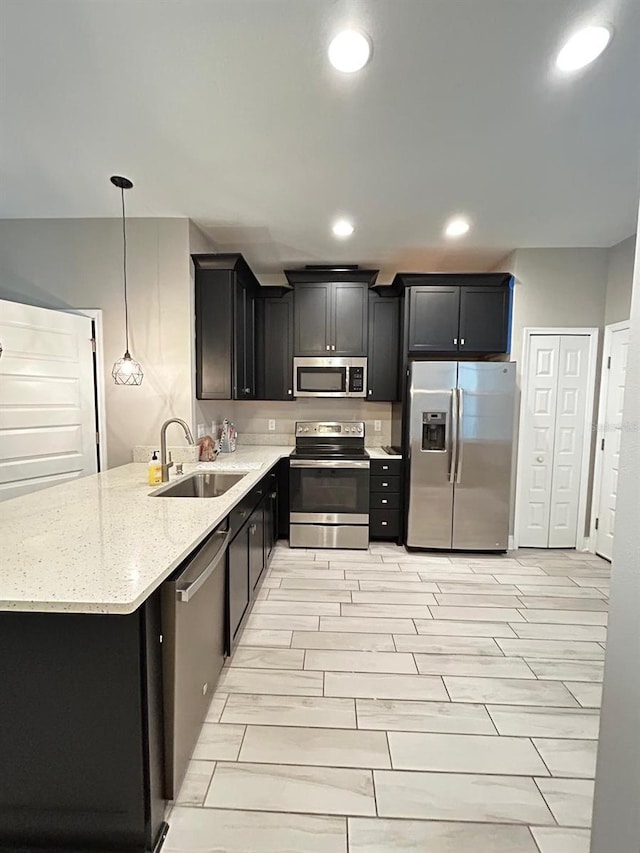 kitchen featuring appliances with stainless steel finishes, pendant lighting, sink, kitchen peninsula, and light stone countertops