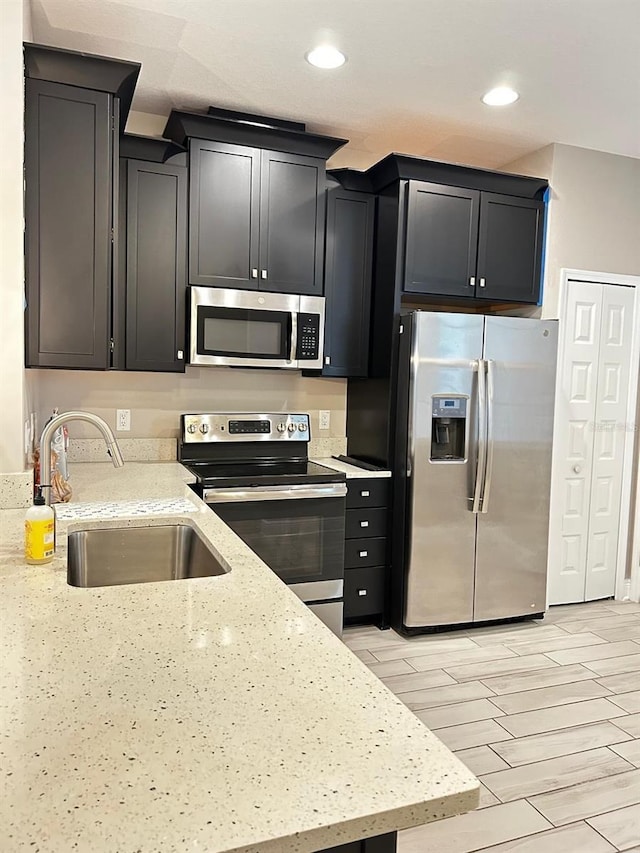 kitchen with appliances with stainless steel finishes, light stone countertops, and sink