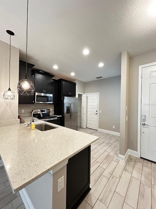 kitchen with sink, light stone counters, kitchen peninsula, pendant lighting, and stainless steel appliances