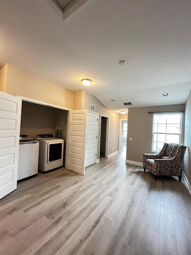 unfurnished living room featuring lofted ceiling, washing machine and clothes dryer, a textured ceiling, and light hardwood / wood-style flooring