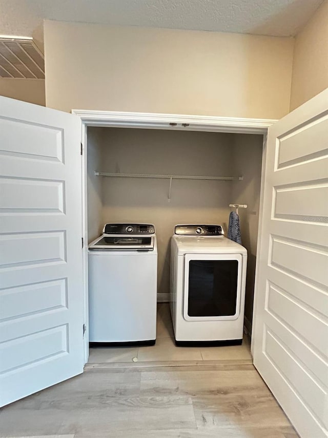 laundry room featuring separate washer and dryer, a textured ceiling, and light wood-type flooring