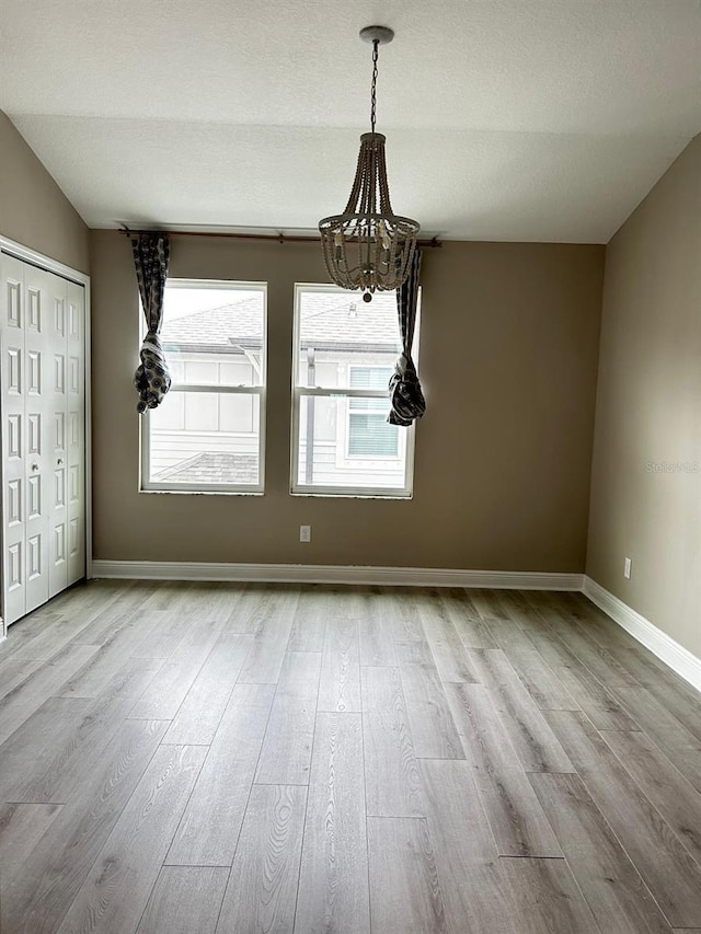 unfurnished dining area with a notable chandelier, vaulted ceiling, a textured ceiling, and light wood-type flooring