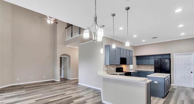 kitchen with pendant lighting, light hardwood / wood-style flooring, blue cabinetry, black appliances, and kitchen peninsula