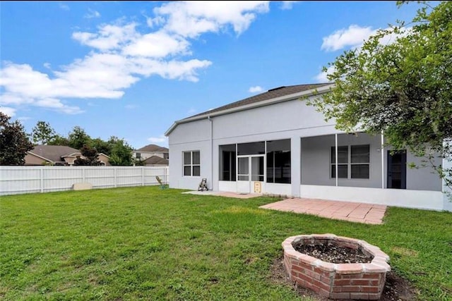 rear view of property featuring a yard, a sunroom, a patio, and an outdoor fire pit