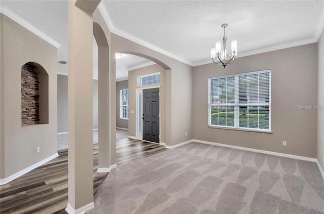 carpeted spare room featuring ornamental molding, a wealth of natural light, and an inviting chandelier