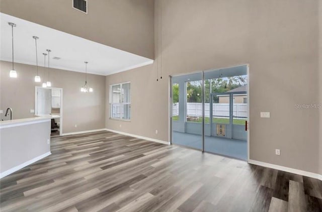 unfurnished living room with an inviting chandelier, hardwood / wood-style floors, a towering ceiling, and ornamental molding