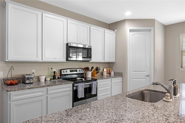 kitchen with light stone counters, stainless steel appliances, sink, and white cabinets