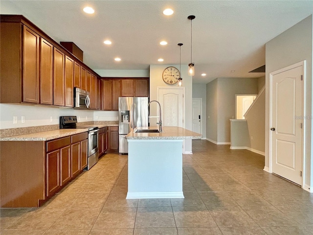 kitchen featuring sink, appliances with stainless steel finishes, hanging light fixtures, light stone countertops, and a center island with sink