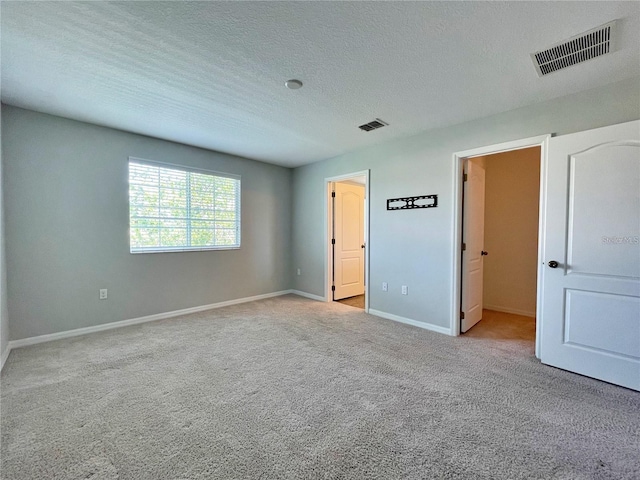 unfurnished bedroom with a spacious closet, light colored carpet, and a textured ceiling