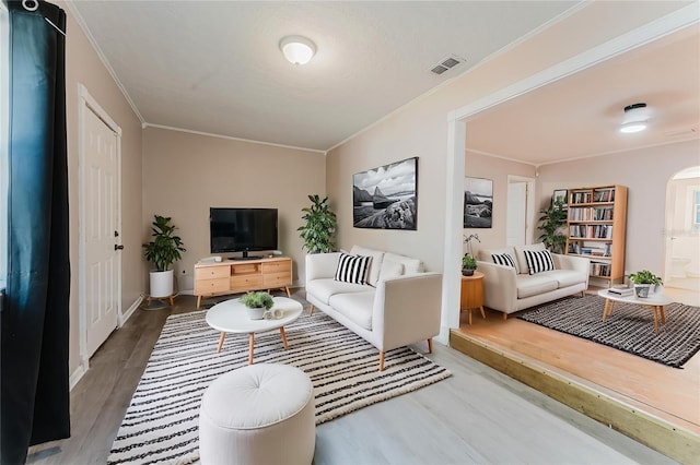 living area featuring visible vents, wood finished floors, baseboards, and ornamental molding