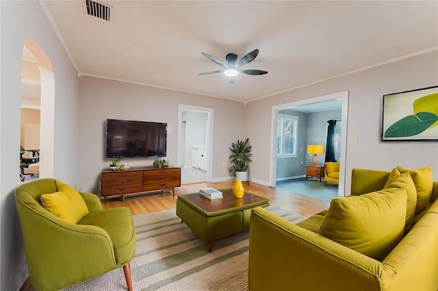 living room featuring light wood finished floors, visible vents, ornamental molding, arched walkways, and a ceiling fan