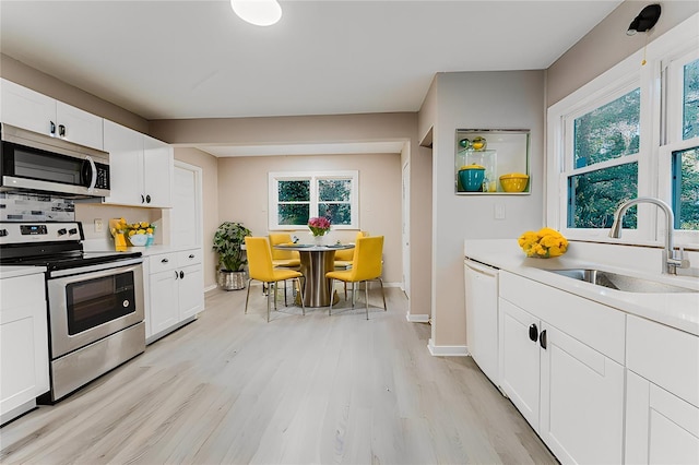 kitchen featuring a sink, white cabinetry, stainless steel appliances, light wood-style floors, and light countertops