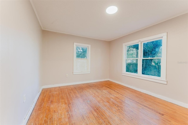 empty room with ornamental molding, baseboards, and light wood-type flooring