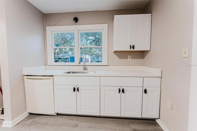 kitchen with a sink, white cabinets, white dishwasher, and light countertops