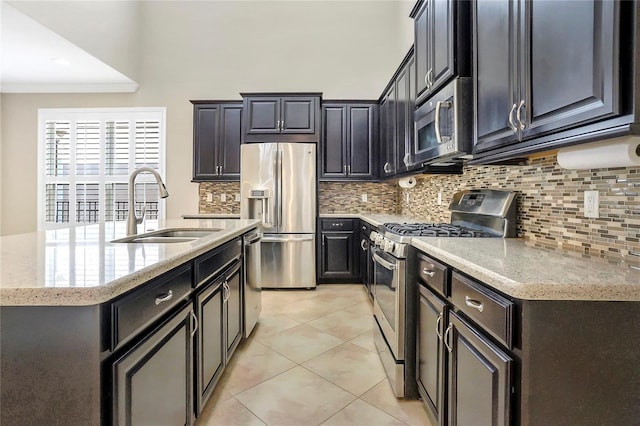 kitchen with light tile patterned flooring, sink, light stone counters, appliances with stainless steel finishes, and an island with sink