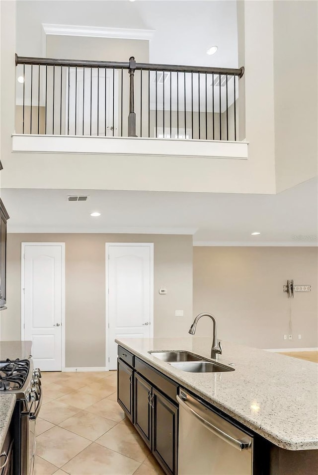 kitchen featuring an island with sink, sink, dark brown cabinetry, stainless steel appliances, and light stone countertops