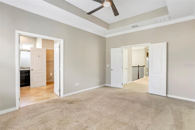 unfurnished bedroom featuring connected bathroom, light colored carpet, a raised ceiling, and ceiling fan