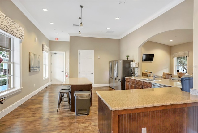 kitchen featuring stainless steel appliances, wood-type flooring, a kitchen bar, decorative light fixtures, and kitchen peninsula