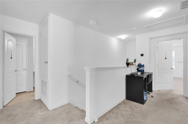 corridor with light colored carpet and a textured ceiling