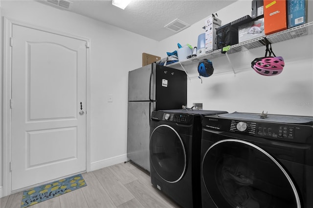 laundry room featuring washing machine and dryer, a textured ceiling, and light hardwood / wood-style flooring