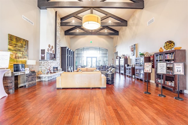 living room with a high ceiling, wood-type flooring, a stone fireplace, and beam ceiling