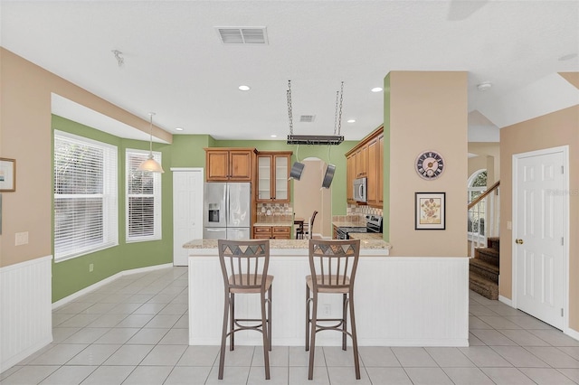 kitchen with light stone counters, light tile patterned flooring, a breakfast bar, and appliances with stainless steel finishes