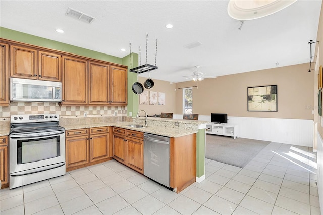 kitchen with stainless steel appliances, sink, light stone counters, and kitchen peninsula