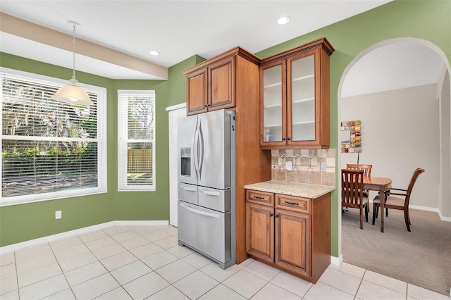 kitchen with light tile patterned flooring, decorative light fixtures, backsplash, stainless steel refrigerator with ice dispenser, and light stone countertops