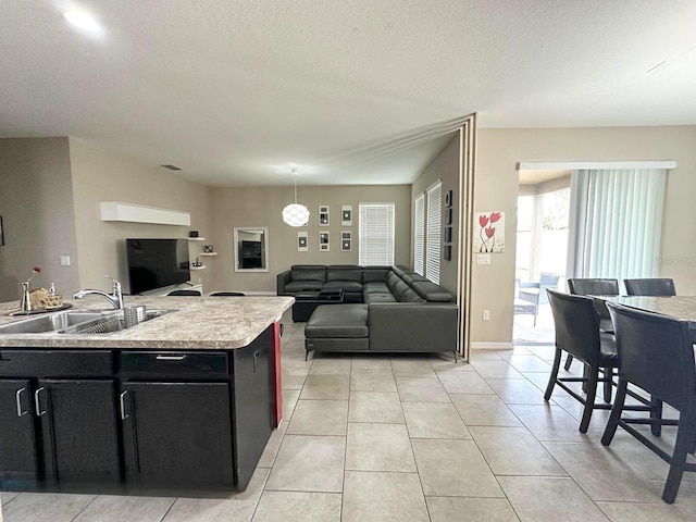 kitchen featuring sink, light tile patterned floors, hanging light fixtures, an island with sink, and a textured ceiling