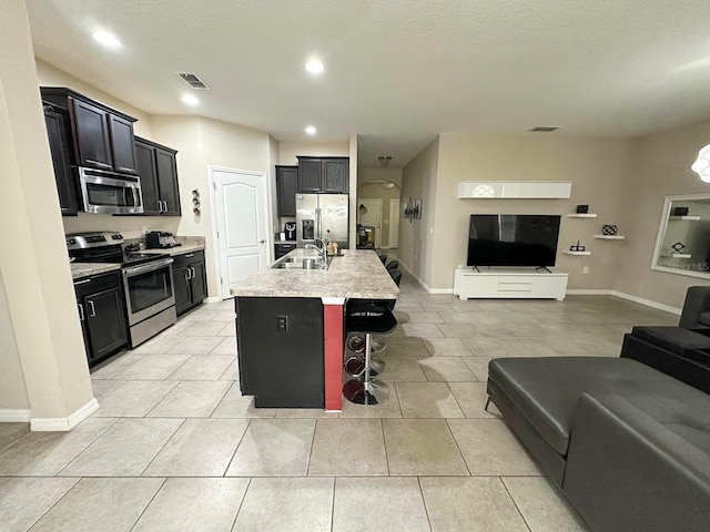 kitchen with sink, light tile patterned floors, appliances with stainless steel finishes, a kitchen island with sink, and a kitchen breakfast bar