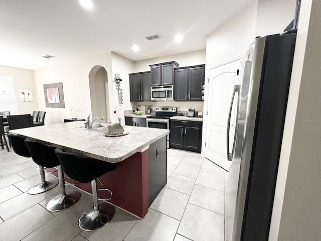 kitchen with sink, light tile patterned floors, stainless steel appliances, a kitchen breakfast bar, and a center island with sink