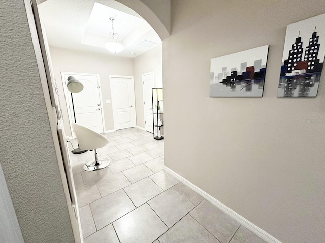 hall with a tray ceiling and light tile patterned floors