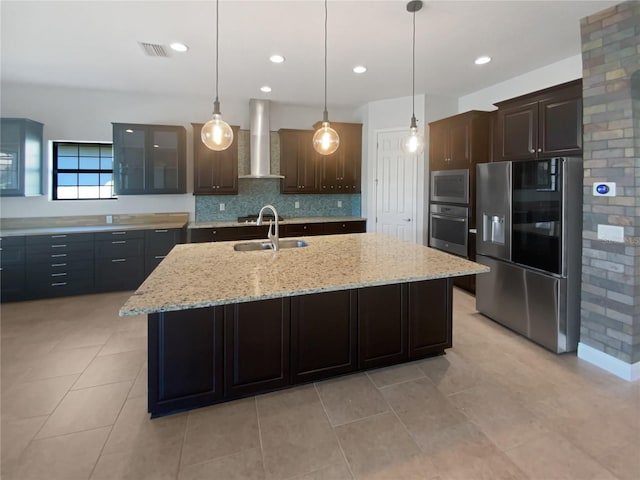 kitchen featuring an island with sink, appliances with stainless steel finishes, dark brown cabinetry, and wall chimney exhaust hood