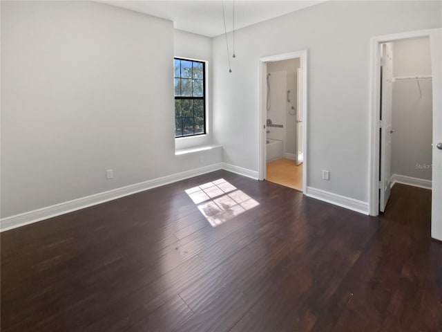 unfurnished bedroom featuring a walk in closet, connected bathroom, dark hardwood / wood-style floors, and a closet