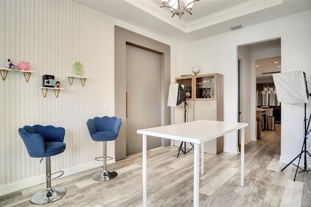 dining room featuring an accent wall, light wood-type flooring, a raised ceiling, and crown molding