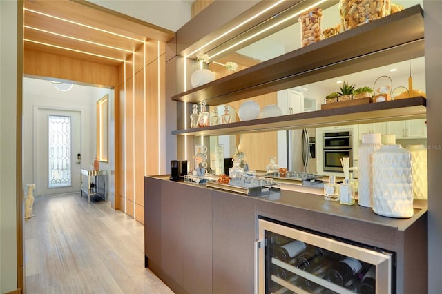 bar with stainless steel appliances, wine cooler, light wood-type flooring, and wet bar