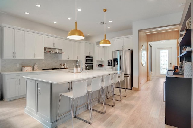 kitchen featuring light wood-type flooring, an island with sink, pendant lighting, stainless steel appliances, and white cabinets