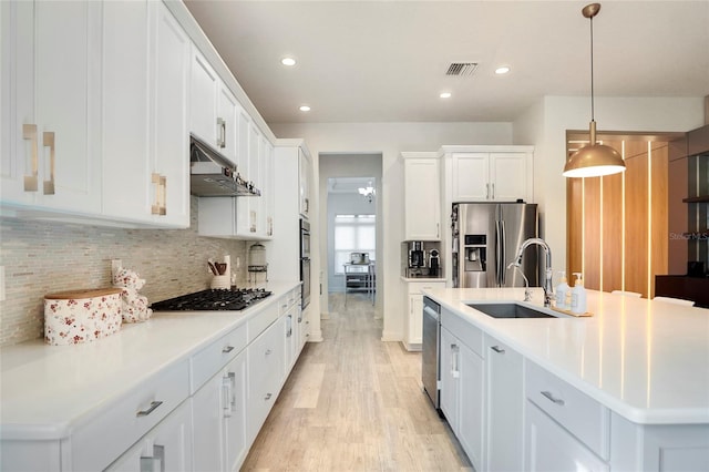 kitchen with decorative light fixtures, a center island with sink, white cabinets, and appliances with stainless steel finishes