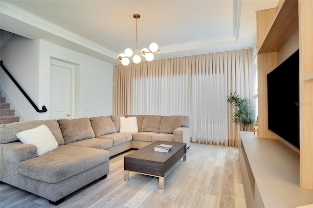 living room with a notable chandelier, a tray ceiling, ornamental molding, and light hardwood / wood-style floors