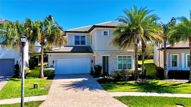 traditional-style home featuring decorative driveway, stucco siding, a front yard, a garage, and stone siding