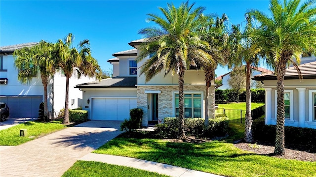 view of front of home featuring decorative driveway, stucco siding, fence, stone siding, and a front lawn