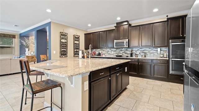 kitchen featuring a breakfast bar, tasteful backsplash, dark brown cabinets, stainless steel appliances, and a kitchen island with sink