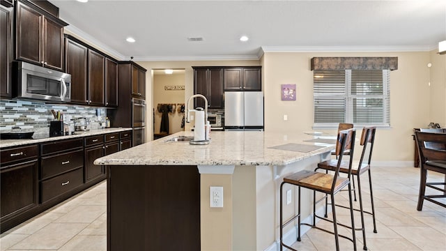 kitchen featuring stainless steel appliances, tasteful backsplash, a center island with sink, and a kitchen breakfast bar