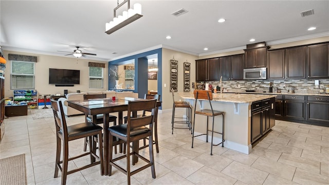 kitchen with pendant lighting, tasteful backsplash, an island with sink, a breakfast bar area, and dark brown cabinetry