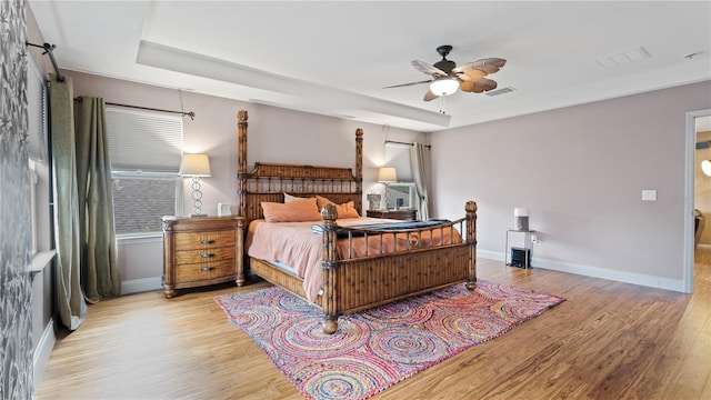 bedroom with a tray ceiling, light hardwood / wood-style flooring, and ceiling fan