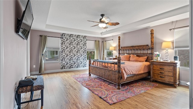 bedroom with ceiling fan, a tray ceiling, and hardwood / wood-style floors