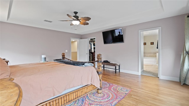 bedroom featuring a walk in closet, light hardwood / wood-style floors, ceiling fan, and ensuite bathroom