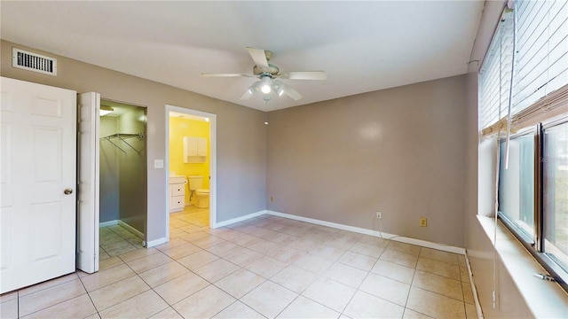 unfurnished bedroom featuring light tile patterned flooring, ceiling fan, connected bathroom, and a walk in closet